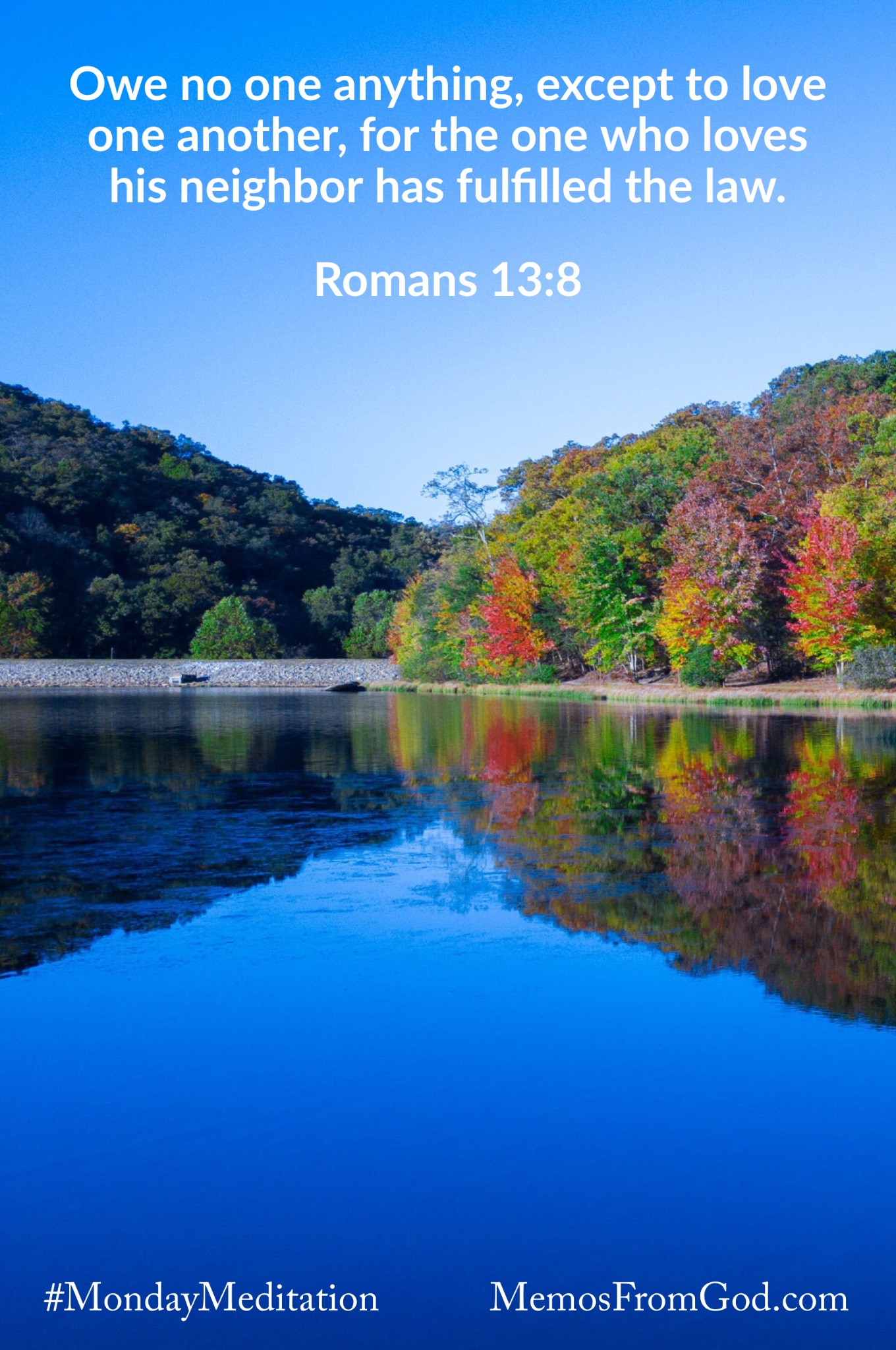 Trees with autumn coloured leaves reflecting in a deep blue lake beneath a bright blue sky. Caption: Owe no one anything, except to love one another, for the one who loves his neighbor has fulfilled the law. Romans 13:8