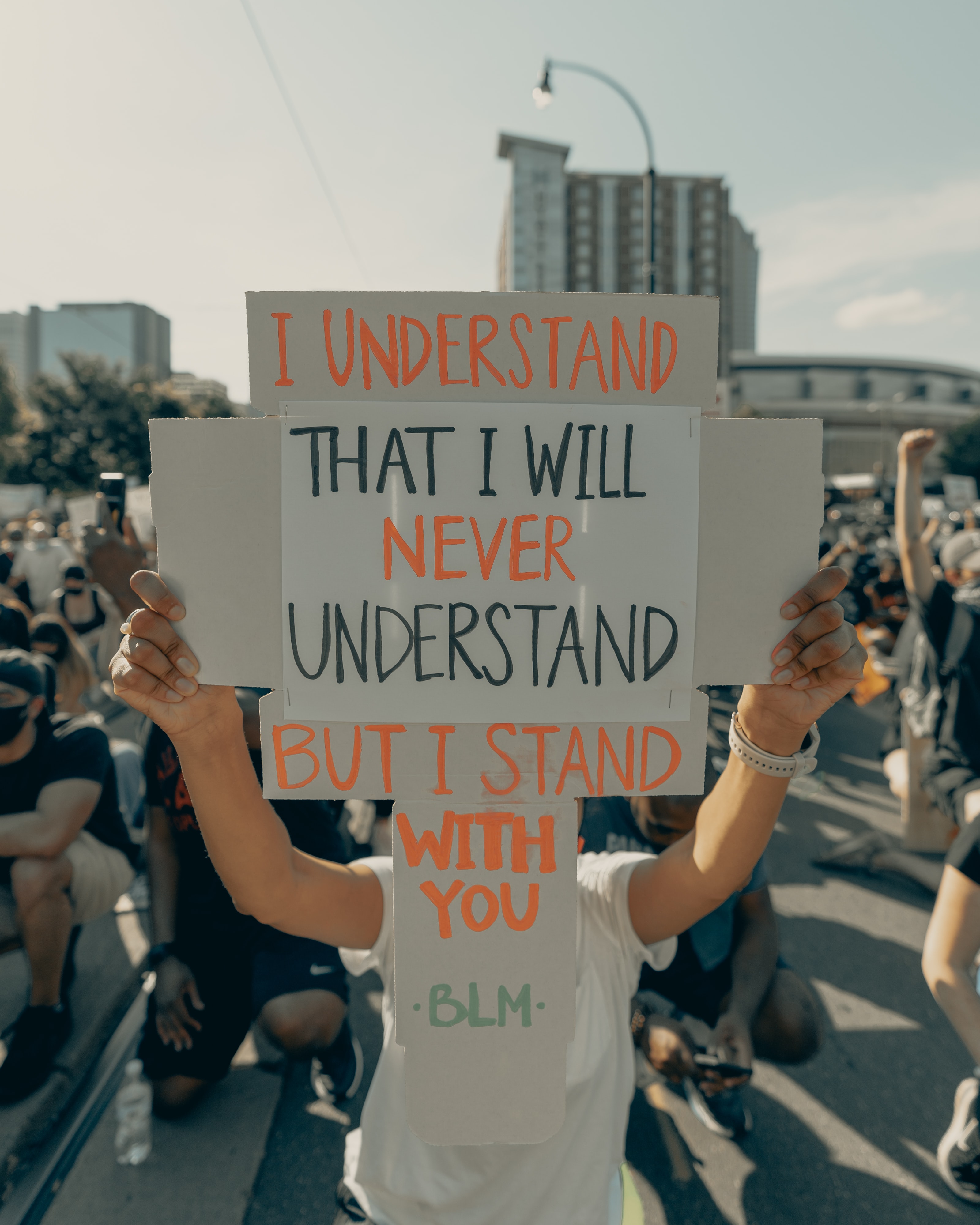 A white person holding a protest sign that says, " I understand that I will never understand, but I stand with you. #BLM"